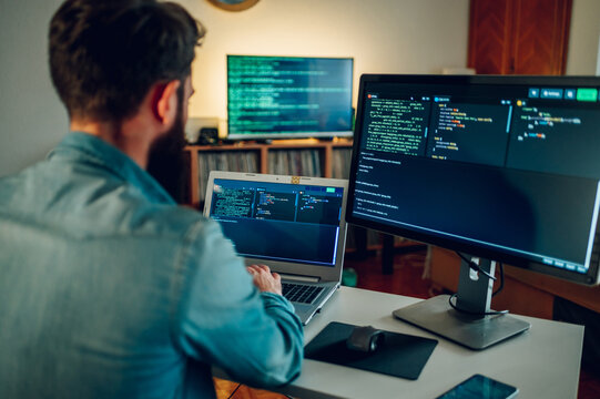 Rear view of a full-stack developer typing code on his laptop at the home office.