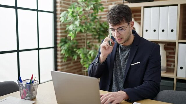 Young hispanic man business worker talking on the phone using laptop at office