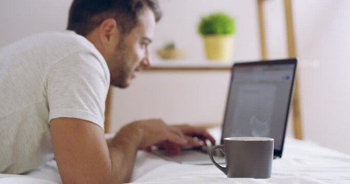 Home, relax and man with a laptop, coffee and typing with connection, search internet and website information. Male person, bedroom and guy with a pc, technology and tea with email and connectivity