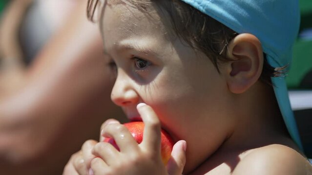 Little boy taking a bite from apple fruit outside during summer day. Pensive cute small child eating healthy snack outdoors in the sunlight