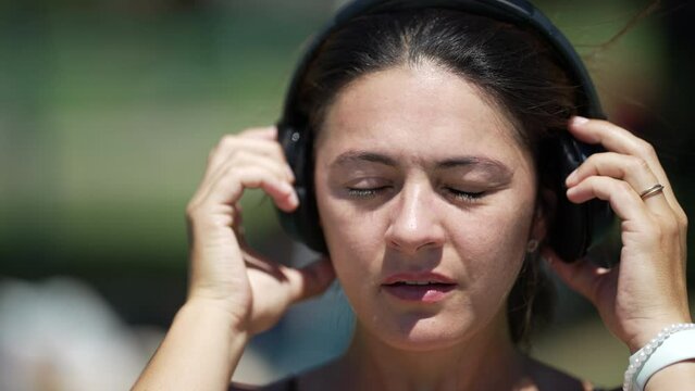 Woman takes off headphones to listen to speaker say something off camera. Female person wearing noise cancelling headphone