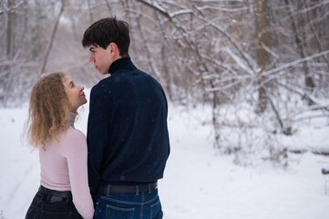 A young couple walks in the park in winter without jackets. Boy and girl hugging on the street. 