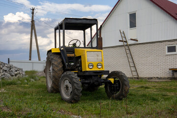 Obraz premium Yellow old tractor on the background of an old house
