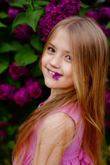 Fototapeta premium close-up of a beautiful blonde girl with big eyes with a lilac flower at the edge of her lips