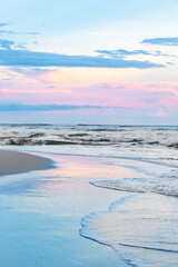 Fototapeta na wymiar Vertical blue and pink ocean beach sunset with waves and sky reflections on the wet sand