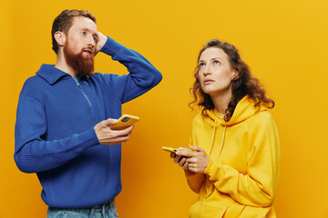 Woman man cheerful couple with phones in hand social networking and communication crooked smile fun and fight, in yellow background. The concept of real family relationships, freelancers, work online.