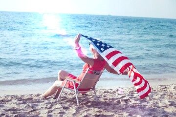 Senior woman holding american flag together on beach, independence day concept
