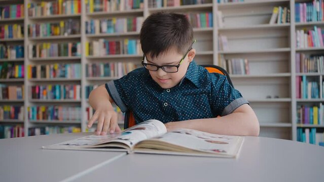 Adorable child boy with trisomy 21 Chromosomes, Down syndrome studying an encyclopedia in library