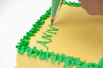 Woman writing with pastry bag on green and yellow birthday cake isolated on white background