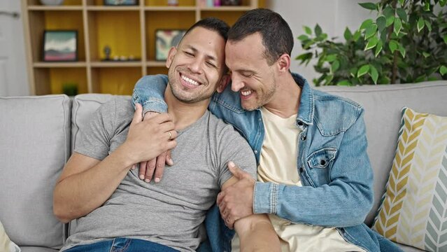 Two men couple hugging each other sitting on sofa at home