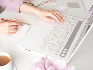 デスクでラップトップを使用しながらメモを取る女性の手元、可愛い女性のワークスペース、オフィス、在宅勤務のコンセプト