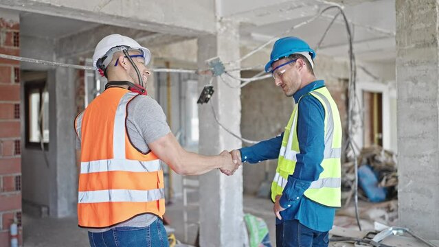 Two men builders shake hands speaking at construction site