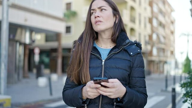 Young caucasian woman using smartphone looking upset at street