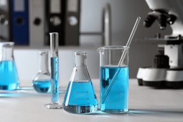 Different laboratory glassware with light blue liquid on table