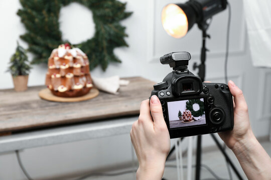 Food photography. Woman with professional camera taking photo of Pandoro cake, Christmas wreath and tree on table in studio, closeup. Space for text