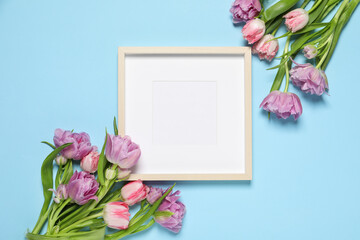 Empty photo frame and beautiful tulip flowers on light blue background, flat lay. Space for design