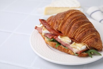 Tasty croissant with brie cheese, ham and bacon on white tiled table, closeup. Space for text