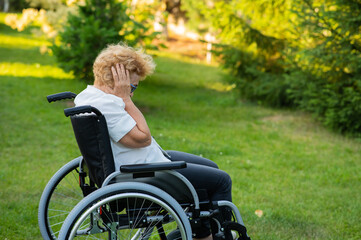 Unhappy elderly woman crying while sitting in a wheelchair on a walk outdoors. 