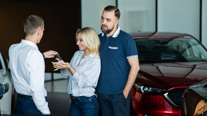 The seller hands over the car keys to the buyers. The couple bought a new car.