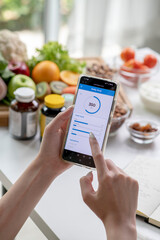Woman professional nutritionist working and checking data from a smartphone with a variety of fruits, nuts, vegetables, and dietary supplements on the table - 606939727