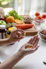 Woman professional nutritionist checking dietary supplements in hand, surrounded by a variety of fruits, nuts, vegetables, and dietary supplements on the table - 606939730