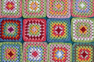 Fototapeta na wymiar Granny squares on blue background. Top view with copy space. Handmade crocheting, needlework and handicraft concept - crocheting accessories