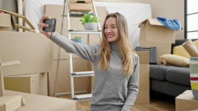 Young caucasian woman sitting on the floor taking selfie by smartphone at new home
