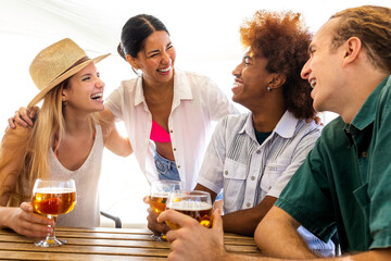 Young happy hispanic woman on vacation having fun with friends in beach bar while having beers together.