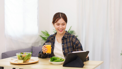 Lifestyle in living room concept, Young Asian woman touching on tablet and drinking orange juice