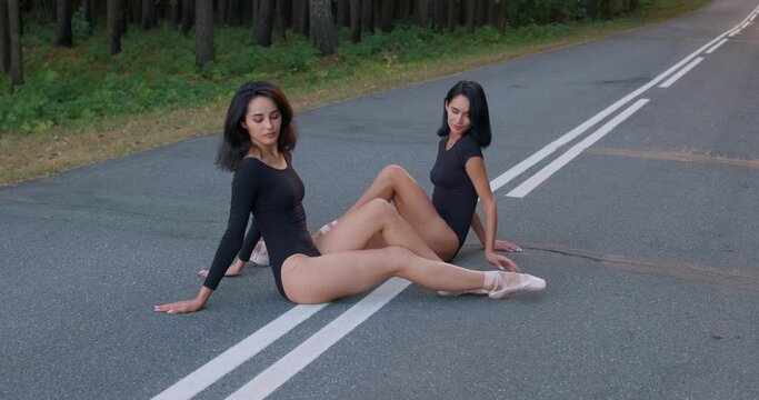 sexy awesome fit sportswomen in suits and pointies sit on road in beautiful landscape in summer, tired slim ballerinas lying on road