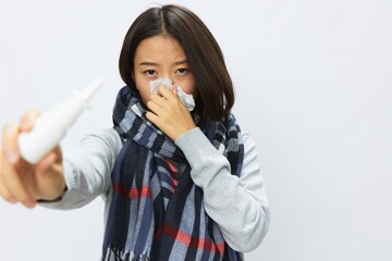 Asian woman flu cold with stuffy nose holds nasal spray shows in camera for allergies with sore throat on white background