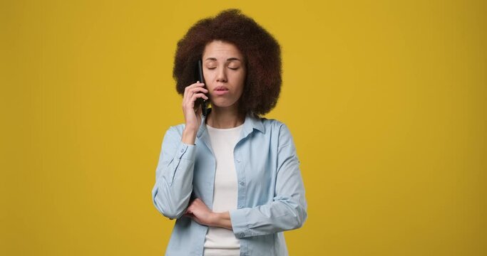 Young beautiful serious frustrated African american woman talking on the phone answering phone call over yellow orange background