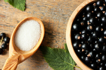Fresh black currant berries lie in a wooden plate next to a spoonful of sugar, healthy eating idea, diet