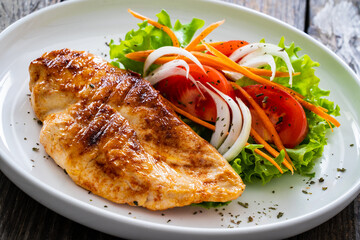 Grilled chicken breast and fresh vegetables on wooden table
