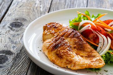Grilled chicken breast and fresh vegetables on wooden table
