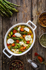 Bread casserole with green asparagus, goat cheese, tomatoes and eggs on wooden table
