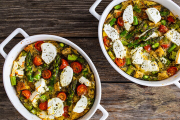 Bread casserole with green asparagus, goat cheese, tomatoes and eggs on wooden table
