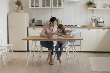 Positive caring grandmother helping little preschool grandkid girl to draw doodles in album, training creative skills, educational activity, spending family leisure at home, doing school homework