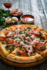 Pizza with cooked ham, mozzarella cheese and vegetables on wooden table
