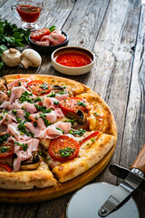 Pizza with cooked ham, mozzarella cheese and vegetables on wooden table