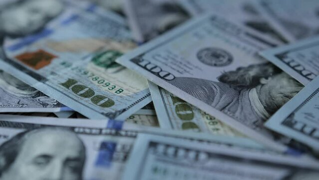 Camera slowly floats over a pile of hundred dollar bills that lie on table blurred background close-up.