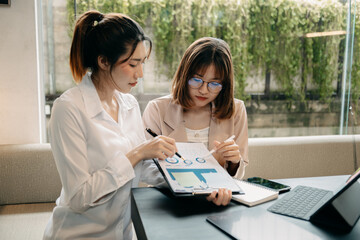 Two Asian businesswoman discuss investment project working and planning strategy with tablet laptop computer in modern office..