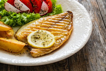 Grilled sea bream with potatoes and fresh vegetables on wooden table
