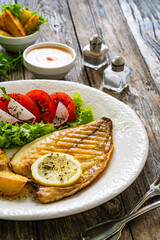Grilled sea bream with potatoes and fresh vegetables on wooden table
