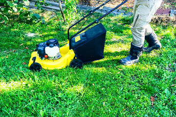 Man mowing lawn with yellow lawn mower in backyard, bright sun