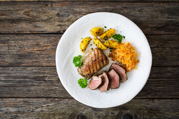 Grilled pork loin steaks with fried potatoes and sauerkraut salad on wooden table
