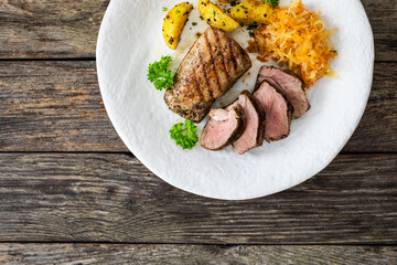 Grilled pork loin steaks with fried potatoes and sauerkraut salad on wooden table
