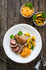 Grilled pork loin steaks with fried potatoes and sauerkraut salad on wooden table
