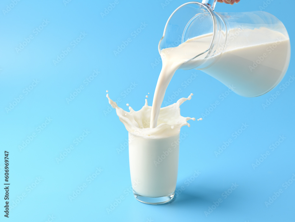 Wall mural pouring fresh milk into the glass with splashing on light blue background.