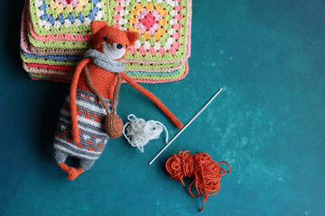 Cute Amigurumi Fox toy. Knitted fox toy with wool yarn and crochet hook on a turquoise background with copy space.  - obrazy, fototapety, plakaty